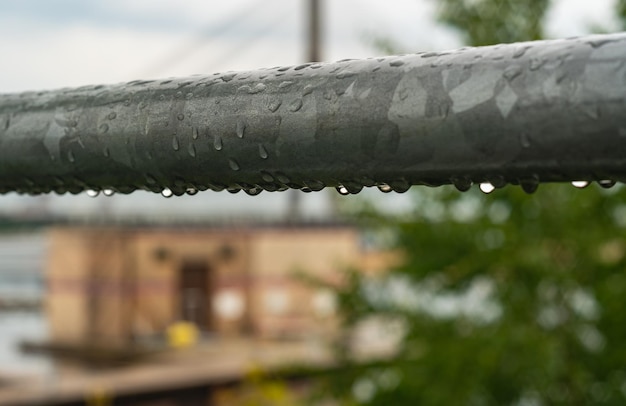 Raindrops on grey metal pipe after rain with house in the background