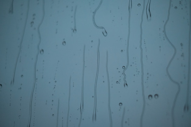 Raindrops trickle down the glass against the evening sky. Raindrops on the window.