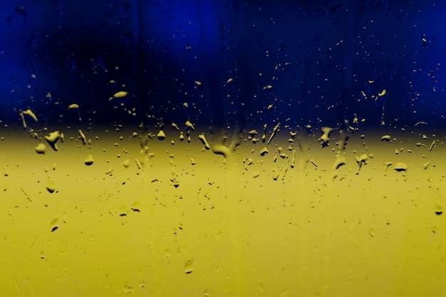 Raindrops on window glass, on blue and yellow background in colors of the Ukrainian national flag