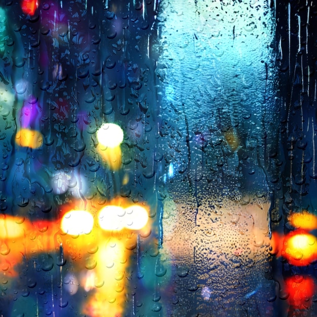 rainy city night car traffic blurred light rain drops on window glass defocus background