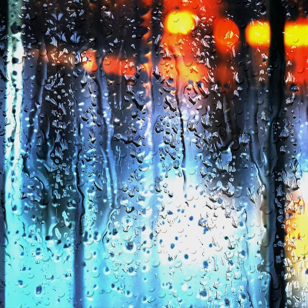 rainy city night car traffic blurred light rain drops on window glass defocus background