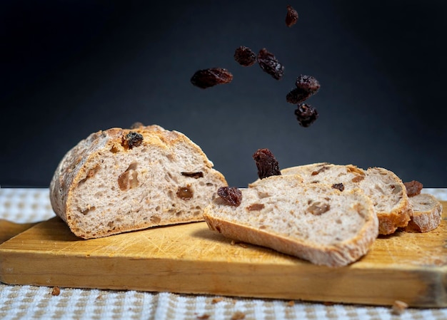 Raisins falling from above onto slices of homemade bread with raisins walnuts spices and chopped nut