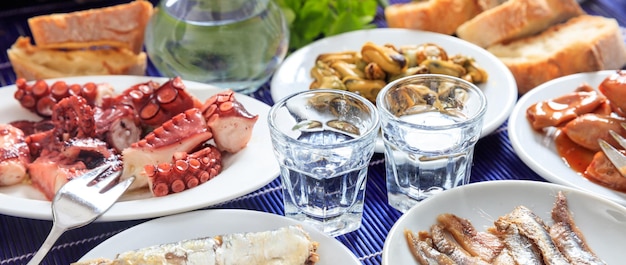 Raki ouzo glasses and seafood appetizers background closeup view