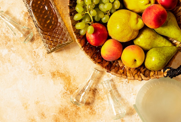 Rakia or Rakija the traditional balkan fruit brandy. The fruits of which produce Rakia. Fruits in a basket, bottles and glasses for alcohol. Top view. Light vintage background. Space for text