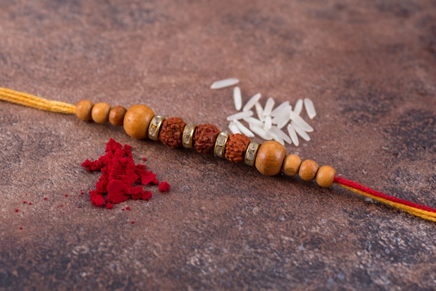 Photo raksha bandhan : rakhi with rice grains and kumkum on stone background