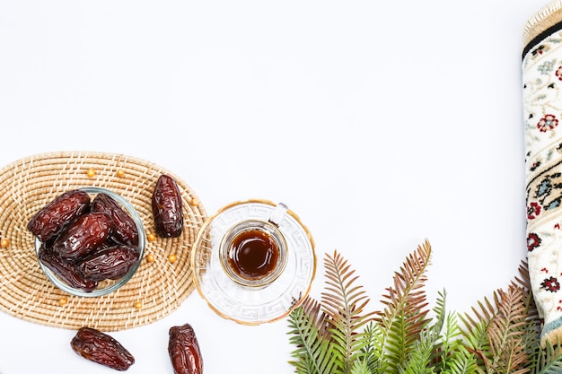 Ramadan inspiration showing date palms in a bowl with tea and prayer mat on a white background