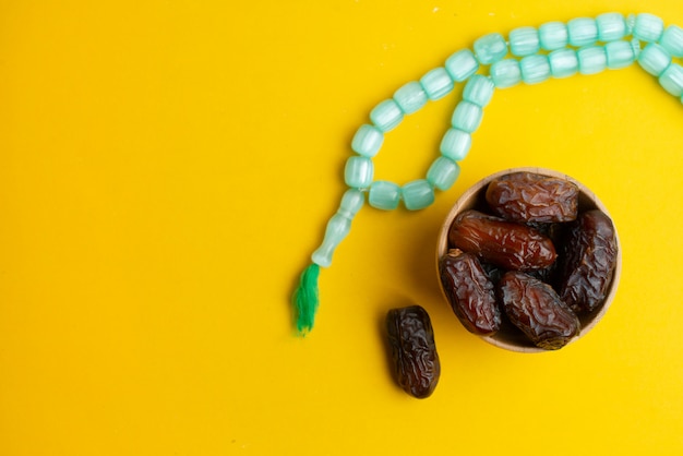 Ramadan Kareem Festival, Dates at wooden bowl with rosary on yellow background