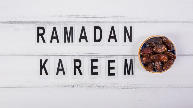 Photo ramadan kareem text with bowl of juicy dates on white desk