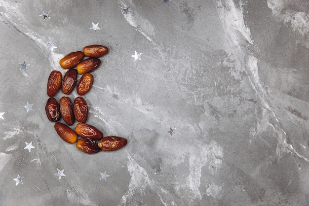 Ramadan kareem with dates fruits arranged in shape of crescent moon isolated on gray stone background top view copy space Iftar food concept