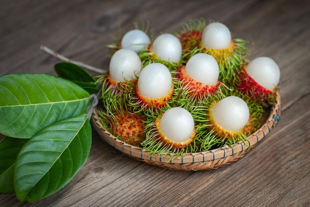 Rambutan fruit harvest from the garden rambutan tree fresh and ripe rambutan sweet tropical fruit peeled rambutan with leaf on wooden basket