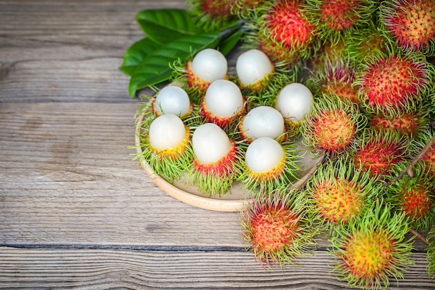 Rambutan fruit harvest from the garden rambutan tree fresh and ripe rambutan sweet tropical fruit peeled rambutan with leaf on wooden plate