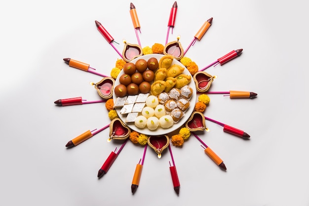 Rangoli or design made using Diya or oil lamp, flowers and sweets likeGulab Jamun, Rasgulla, kaju katli, morichoor or Bundi Laddu, Gujiya or Karanji for diwali celebration