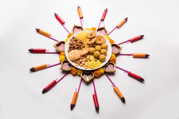 Rangoli or design made using Diya or oil lamp with Indian snacks or sweet and firecrackers or patakhe for Diwali festival