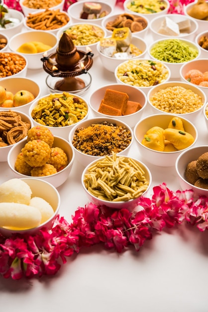 Photo rangoli of sweets and farsan or snacks in bowls for diwali with diya over white background