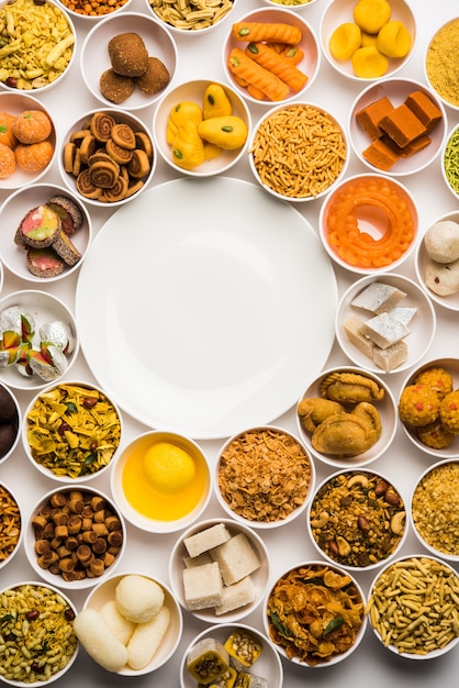 Rangoli of sweets and Farsan or snacks in bowls for Diwali with diya over white background