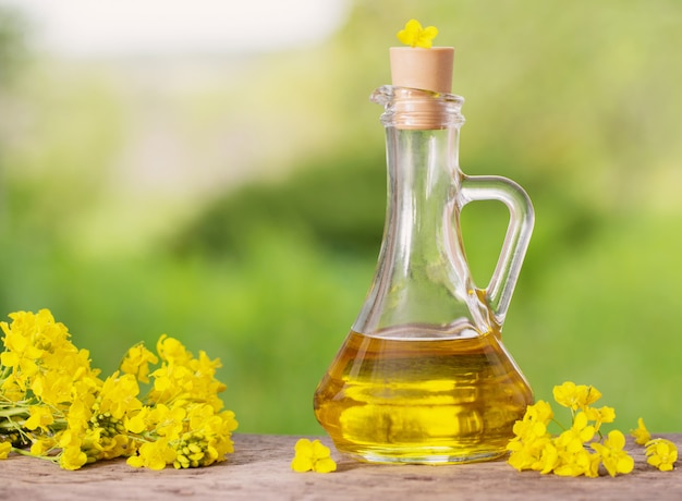 Rapeseed oil (canola) and rape flowers on wooden table