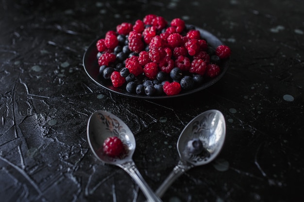 Raspberries and blueberries, on a black background, wild berry