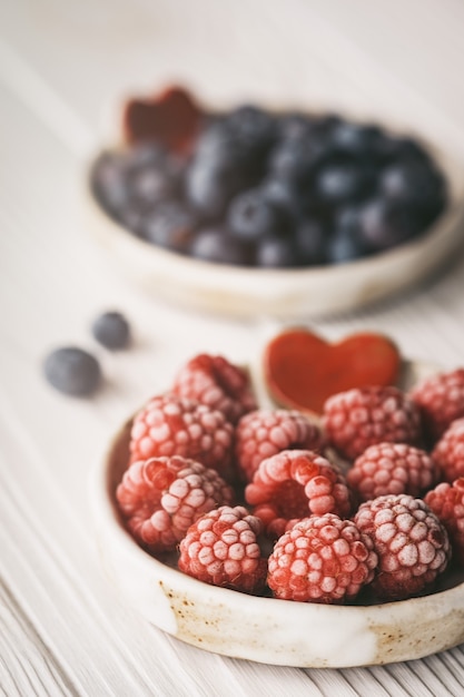 Raspberries and blueberries in small ceramic bowls with red heart decor