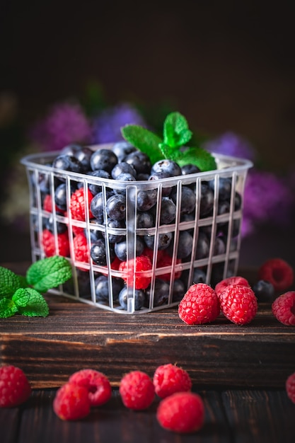 Raspberries and blueberry in a basket on a dark background. Summer and healthy food concept. Background with copy space. Selective focus.