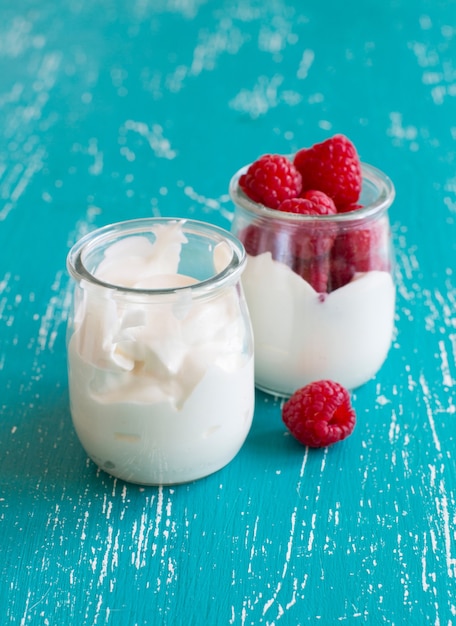 Raspberries and fresh yogurt in a jar on a turquoise table close up