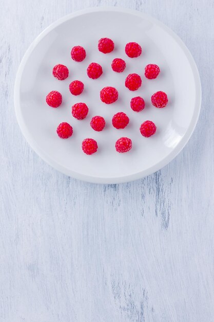 Raspberries on white plate Red raspberry berries on white background Top view Copy space