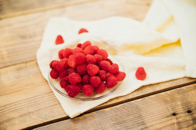 Raspberry fruits on a small saucer a bunch of summer berries on a wooden background Summer background Juicy appetizer or dessert