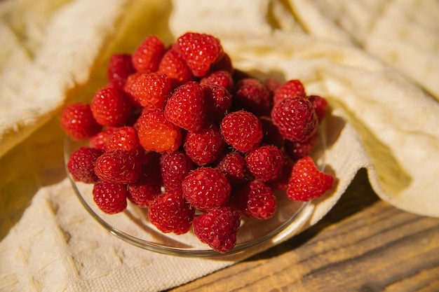 Raspberry fruits on a small saucer a bunch of summer berries on a wooden background Summer background Juicy appetizer or dessert