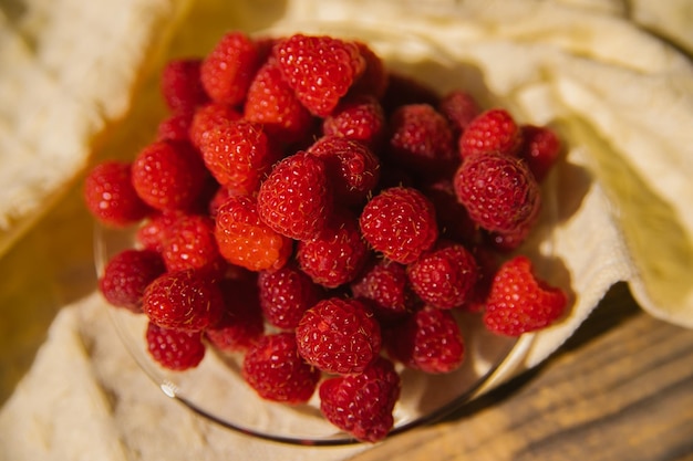 Raspberry fruits on a small saucer a bunch of summer berries on a wooden background Summer background Juicy appetizer or dessert