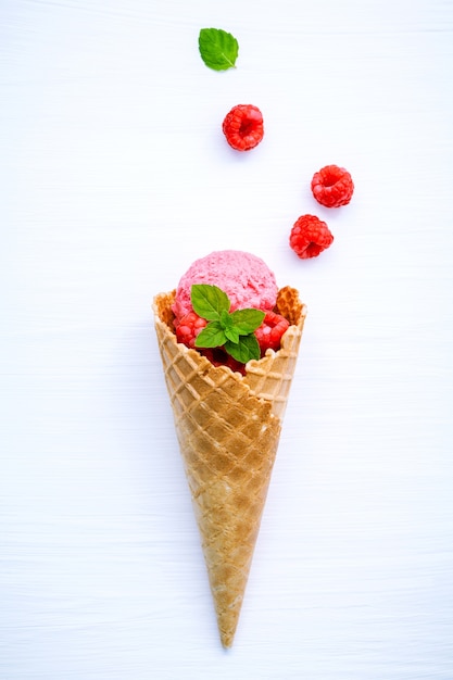 Raspberry ice cream in cone with fresh raspberry setup on white wood background . 