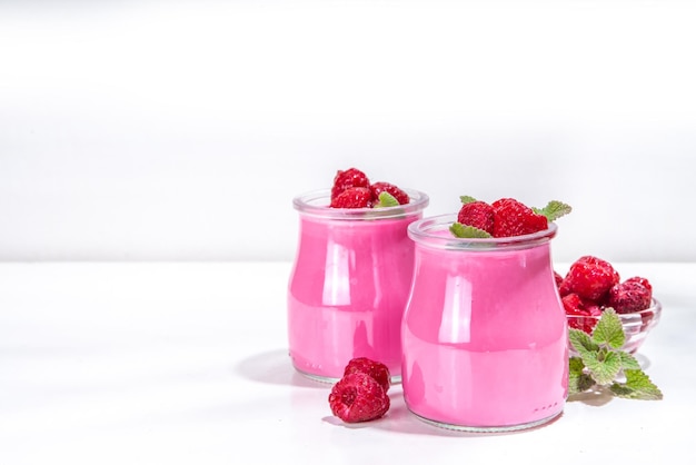 Raspberry panna cotta dessert with fresh raspberries and melissa mint leaves Pink panna cotta in small portion jars on a white background