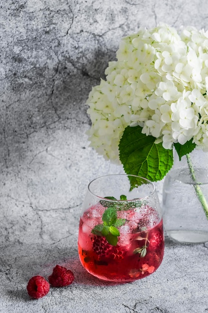 Raspberry peach mint cocktail lemonade refreshing drink and flowers on a gray background