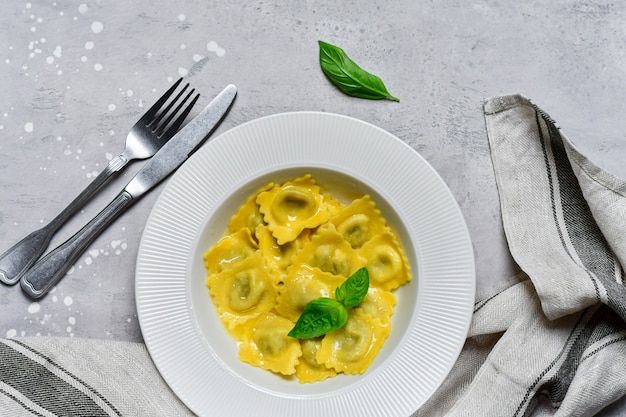 Ravioli with ricotta and spinach in a white plate on a grey stone table. Recipe of Italian pasta, gourmet lunch. Top view