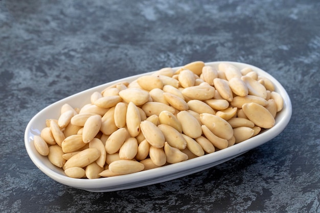 Raw almonds on plate on dark background