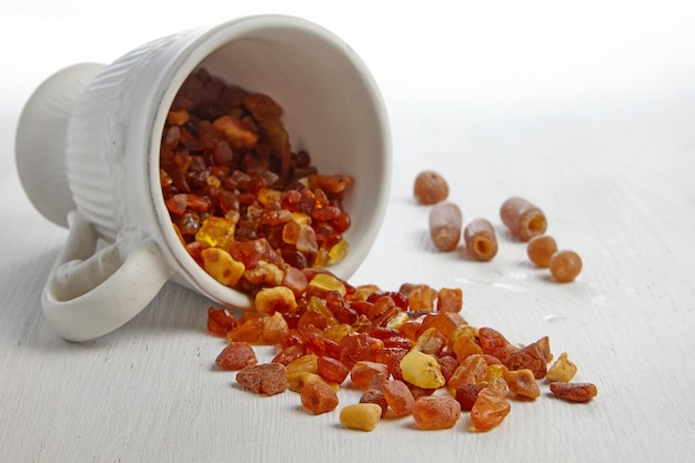 Raw amber spilled out on a wooden table from a white ceramic cup