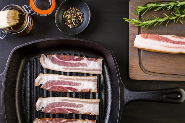 Raw bacon strips on a cast iron frying pan.