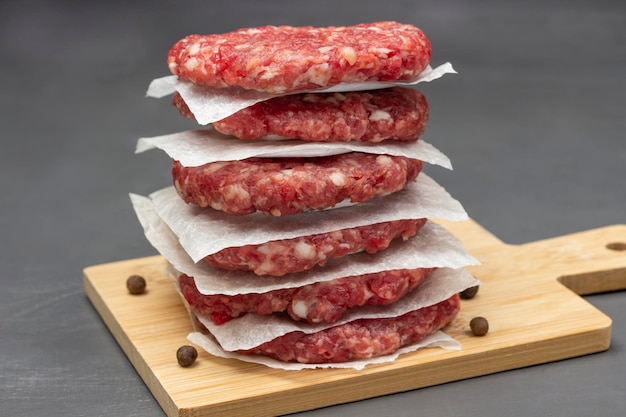 Raw beef burgers are stacked on board Close up