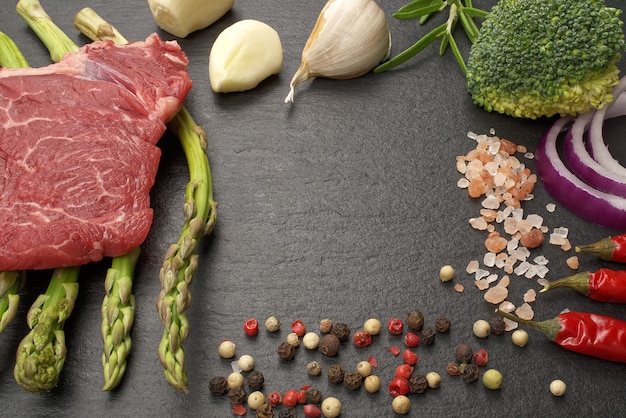 Raw beef fillet on black stone board with asparagus and dry spices ready to cooking