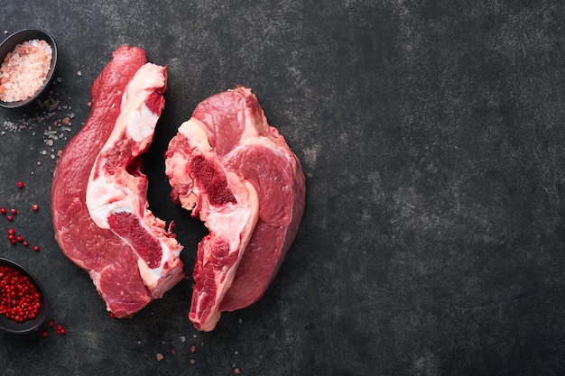 Raw beef meat Rough piece of meat on bone for roast or soup with salt pepper thyme and rosemary on a black concrete background Entrecote Raw cowboy steak Top view