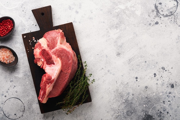 Raw beef meat Rough piece of meat on bone for roast or soup with salt pepper thyme and rosemary on old grey concrete table background Entrecote Raw cowboy steak Top view