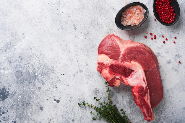 Raw beef meat Rough piece of meat on bone for roast or soup with salt pepper thyme and rosemary on old grey concrete table background Entrecote Raw cowboy steak Top view