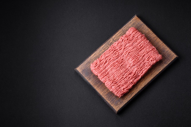 Raw beef or pork mince with salt spices and herbs on a wooden cutting board on a dark concrete background