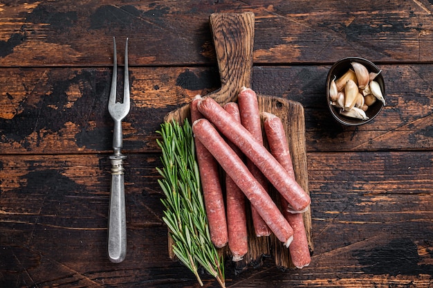 Raw beef and pork sausage on old cutting board with vintage meat fork.