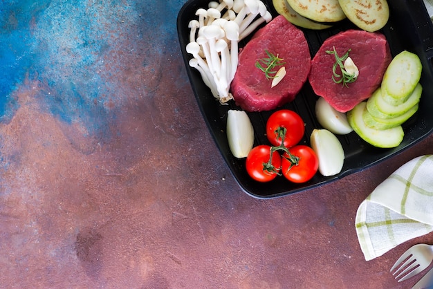 Raw beef steak on the bone with fresh vegetables in a grill pan on concrete 