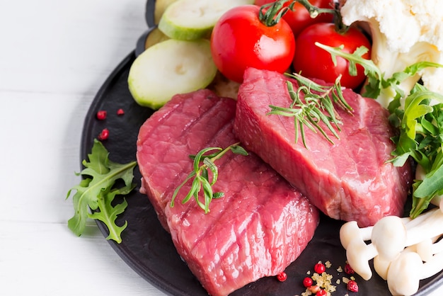 Raw beef steak on the bone with fresh vegetables in a pan on a marble , top view