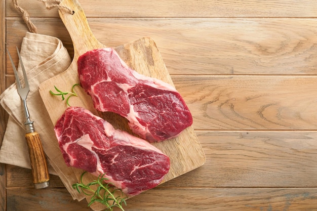 Raw beef steak Marbled raw fresh Ribeye steak with rosemary salt and pepper on cutting board on light old wooden background Raw beef steak and spices for cooking Mock up