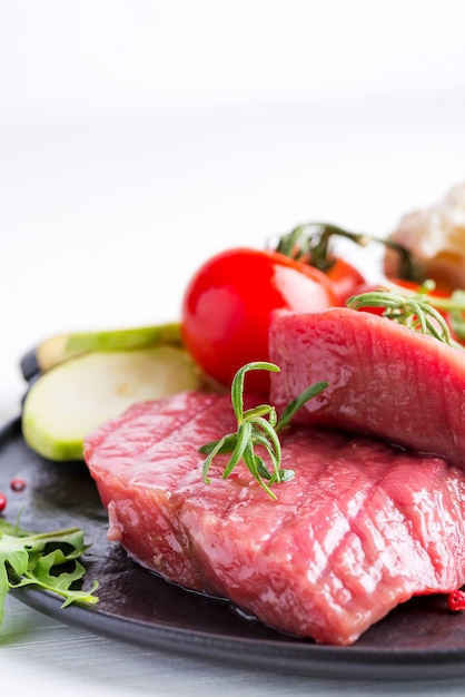 Raw beef steak with fresh vegetables in a pan on a marble background