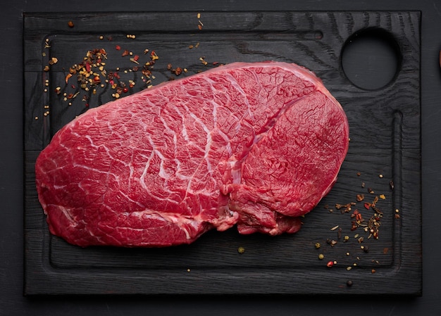 Raw beef tenderloin lies on a brown wooden board black table