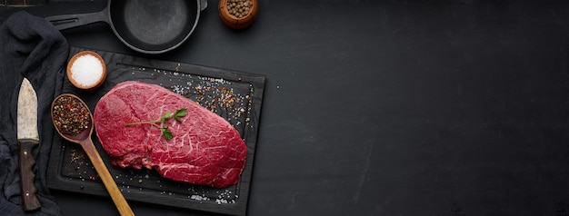 Raw beef tenderloin lies on a brown wooden board black table