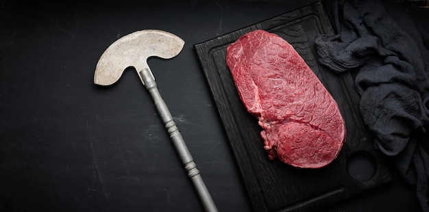 Raw beef tenderloin lies on a cutting board on a black table top view