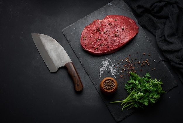 Raw beef tenderloin lies on a cutting board and spices for cooking on a black table top view